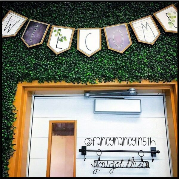 Modern Farmhouse Classroom Decor Bundle - Welcome Banner Shows a Welcome Banner set up on faux grass above a classroom door. The banner include farmhouse designs such as a chalkboard, weathered wood, and wooden borders