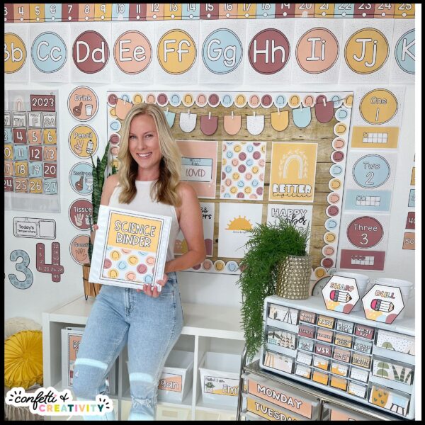 Modern Neutral Classroom Decor - Megan in Classroom Shows the entire classroom decorated in the modern neutral classroom theme. Megan is in the middle of the room holding a binder decorated with the neutral binder cover. She's wearing a white tank top that fits with the color scheme of the neutral classroom