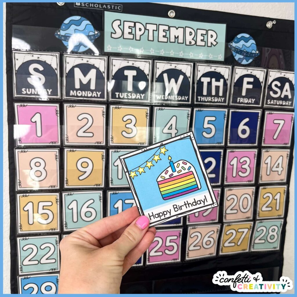 Shows the classroom calendar in a black pocket chart, while holding a holiday card for a birthday